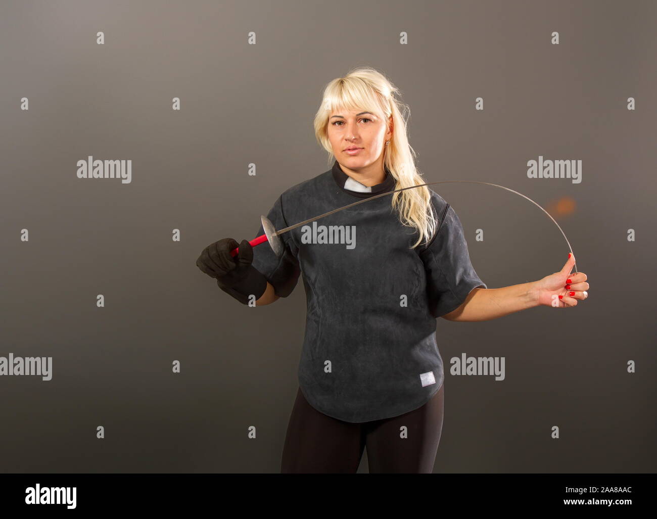 Giovane ragazza bionda in un recinto di coaching uniforme scuro stand con una piattina di pinza su sfondo grigio Foto Stock