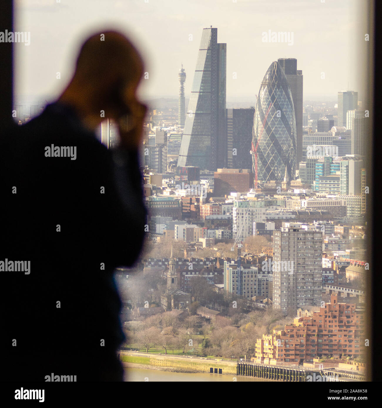 London, England, Regno Unito - 27 Febbraio 2015: un uomo di affari di effettuare una chiamata su un telefono cellulare si stagliano nella finestra di un ufficio Docklands grattacielo, Foto Stock