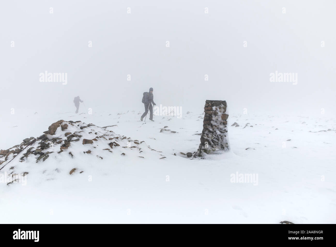 Due escursionisti in condizioni di tempo di inverno avvicinarsi al vertice Trig del pilastro, Lake District, Cumbria, Regno Unito Foto Stock