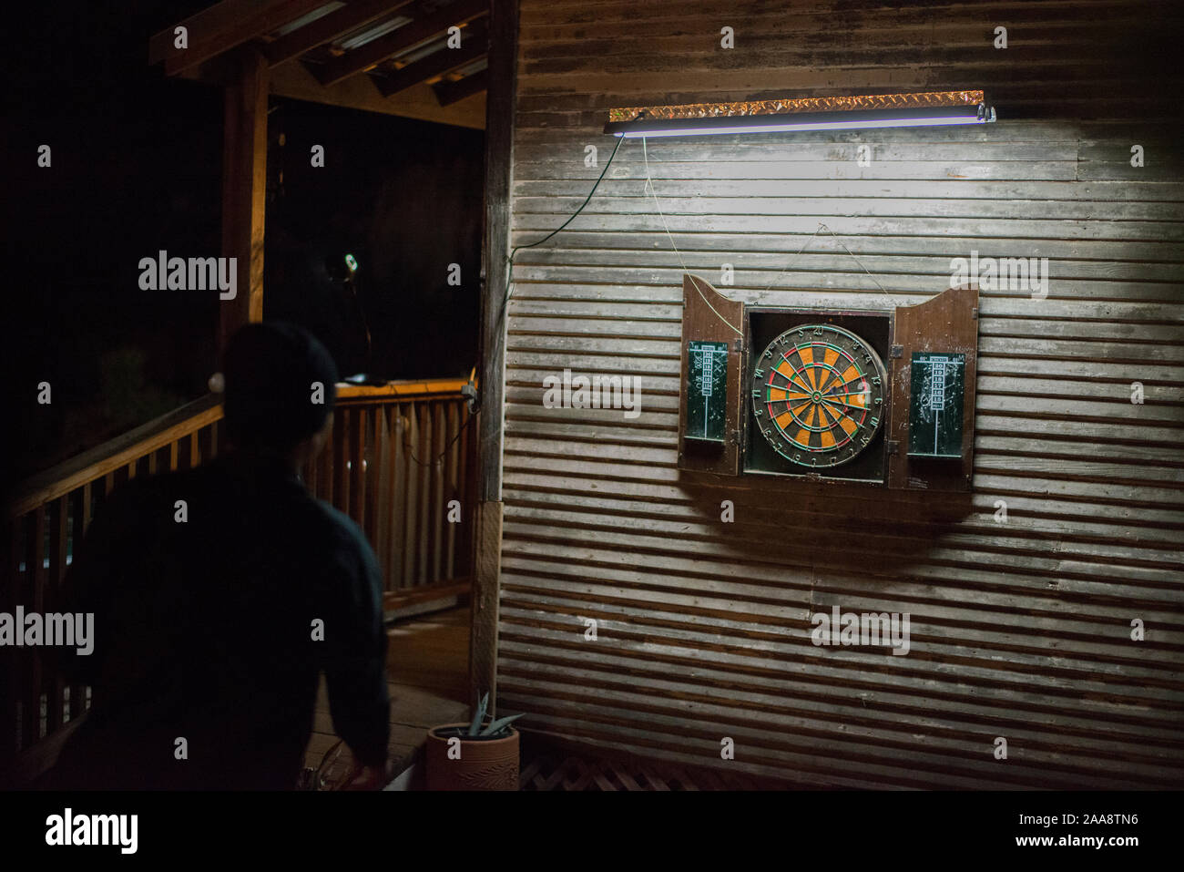 Giovane maschio prestando freccette di notte su un rustico patio esterno Foto Stock