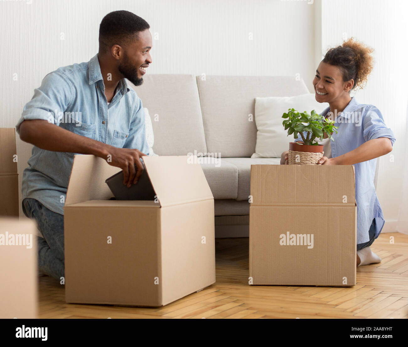 Afro coniugi scatole da imballaggio insieme seduta sul pavimento a casa Foto Stock