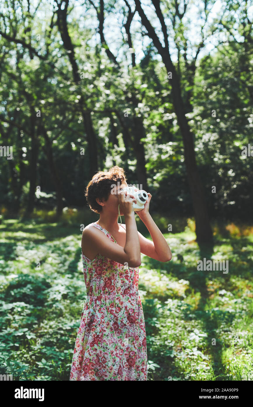 Entusiasta ragazza preteen sollevamento fotocamera istantanea e prendendo la foto in parco verde Foto Stock