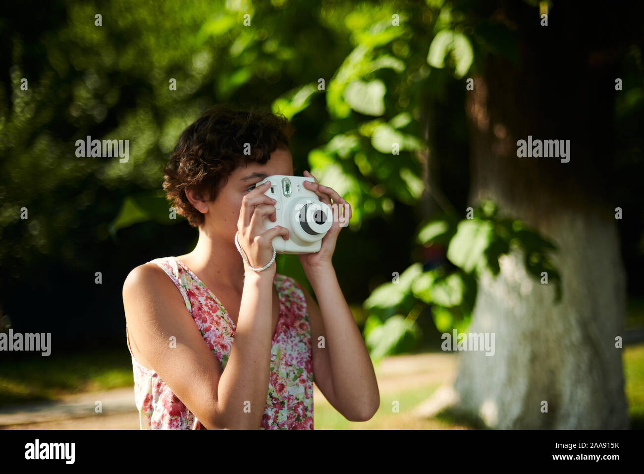 Entusiasta ragazza preteen sollevamento fotocamera istantanea e prendendo la foto in parco verde Foto Stock