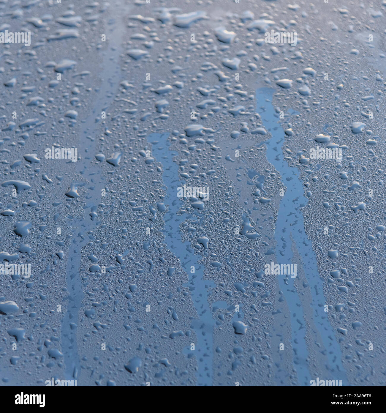 Gocce di pioggia sulla superficie lucida del cofano dell'auto dopo una doccia a pioggia e un cielo blu riflettente sopra. Metafora commercio di acqua, acqua come merce. Foto Stock