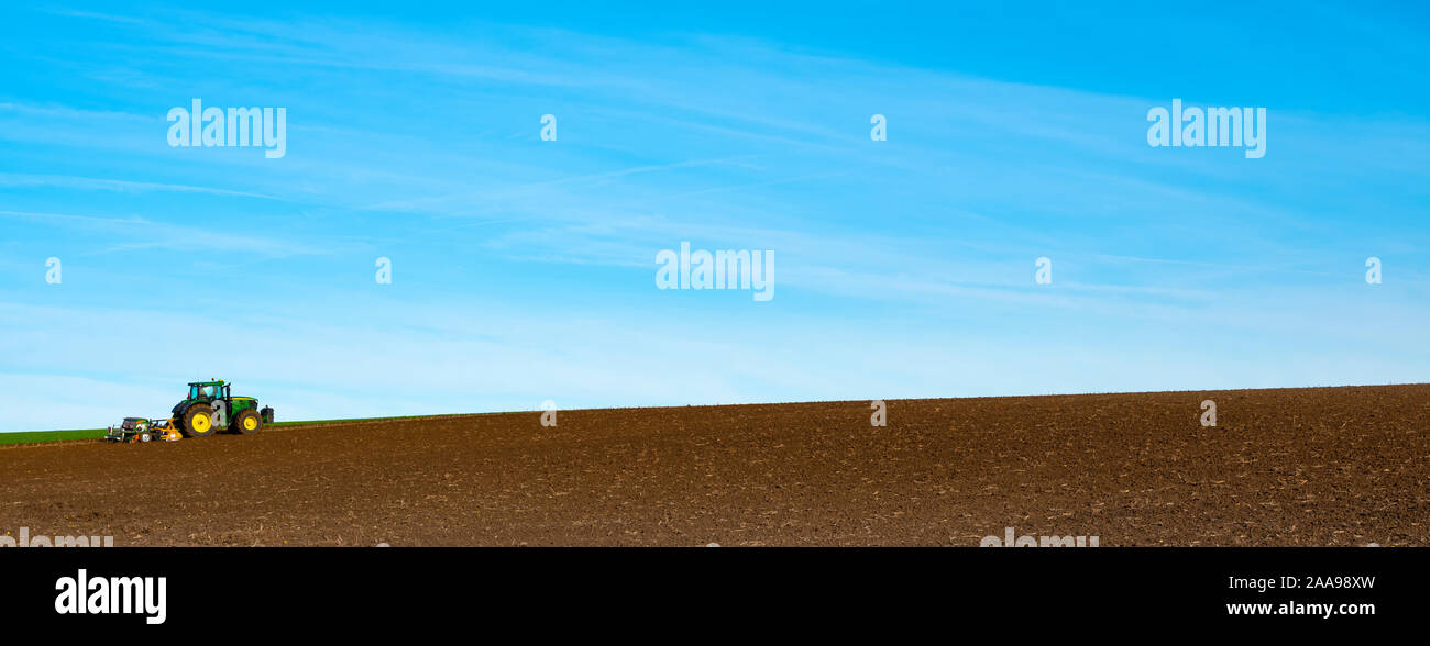 Il trattore funziona grande campo arato sulla collina con erpice sotto il cielo blu nei Paesi Bassi Foto Stock
