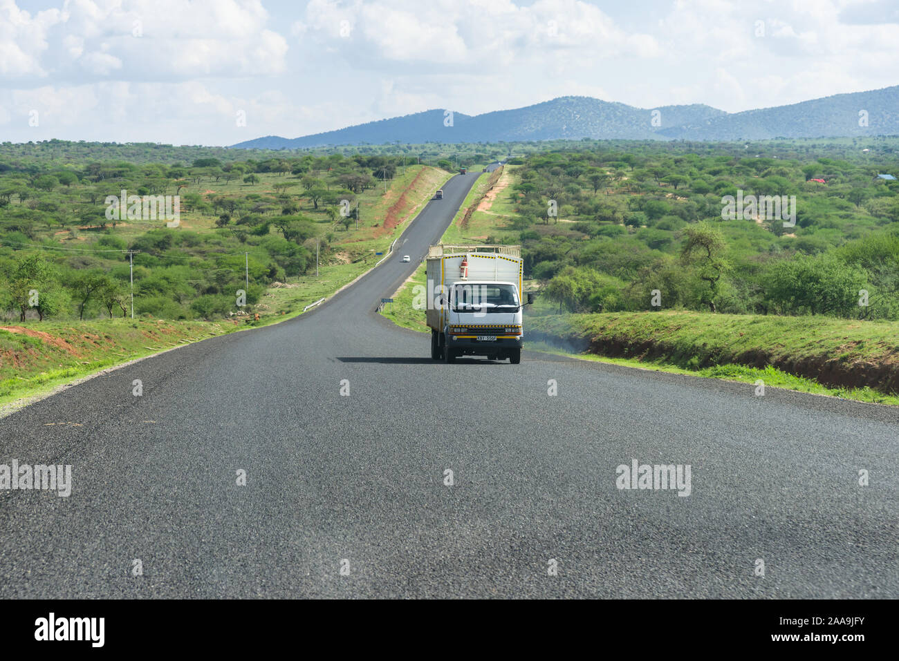Una sezione di Namanga Road verso la Tanzania con un autocarro che passa da alberi, Kenya Foto Stock