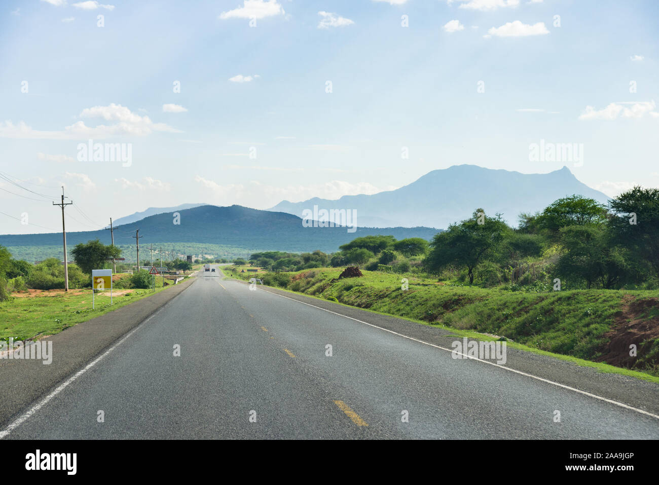 Una sezione di Namanga Road verso la Tanzania fiancheggiata da alberi e colline in background, Kenya Foto Stock
