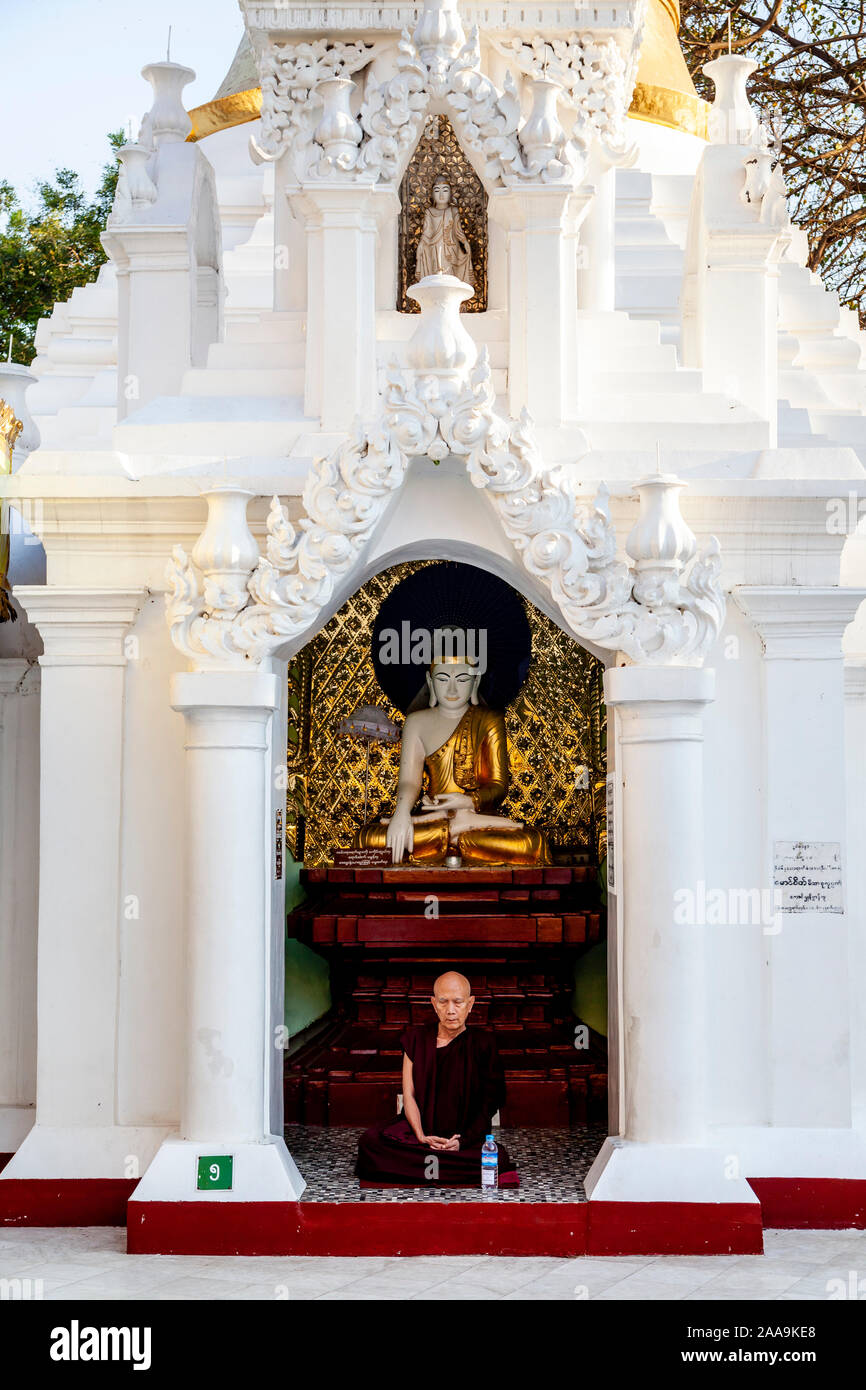 Un monaco buddista seduto di fronte a una statua, la Shwedagon pagoda Yangon, Myanmar. Foto Stock