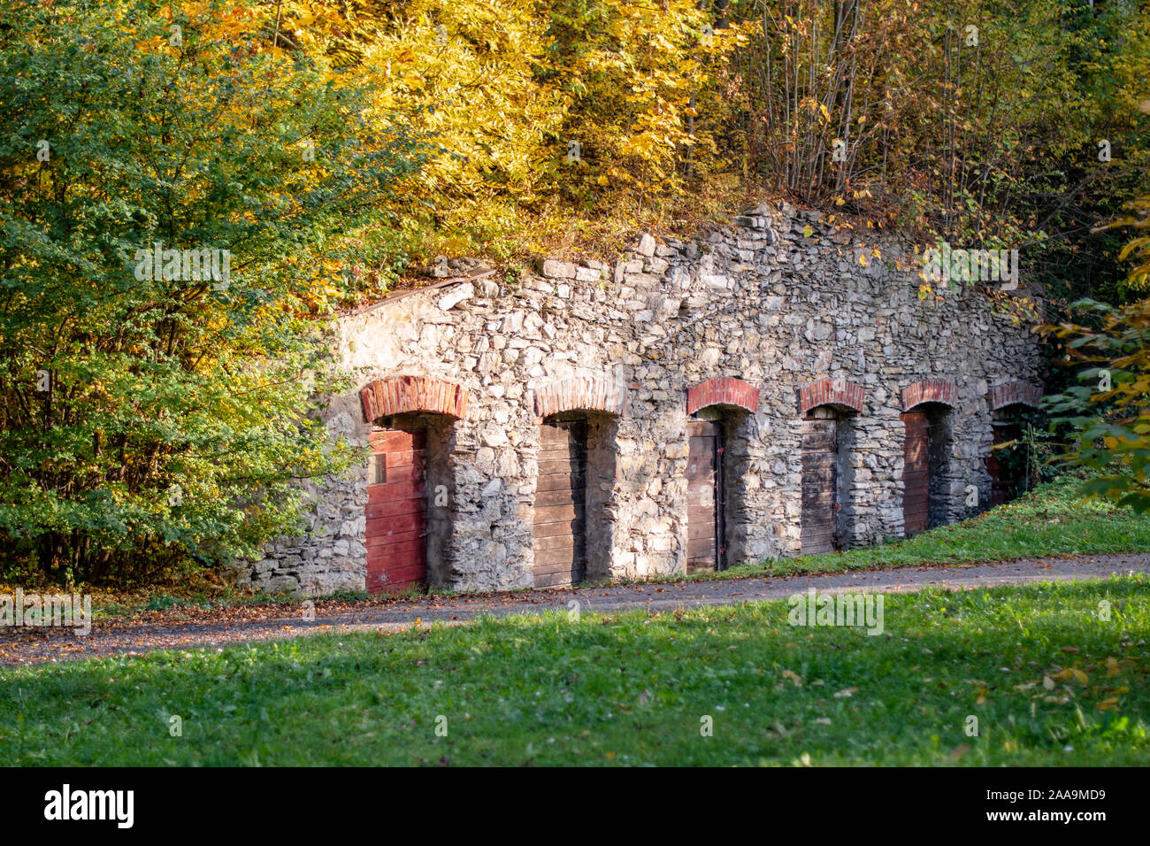 Vecchio muro in pietra con vecchie porte in legno nel parco pubblico in autunno. Posto per nascondersi all'aperto. Nascondiglio nel parco. Deposito abbandonato in collina. Foto Stock