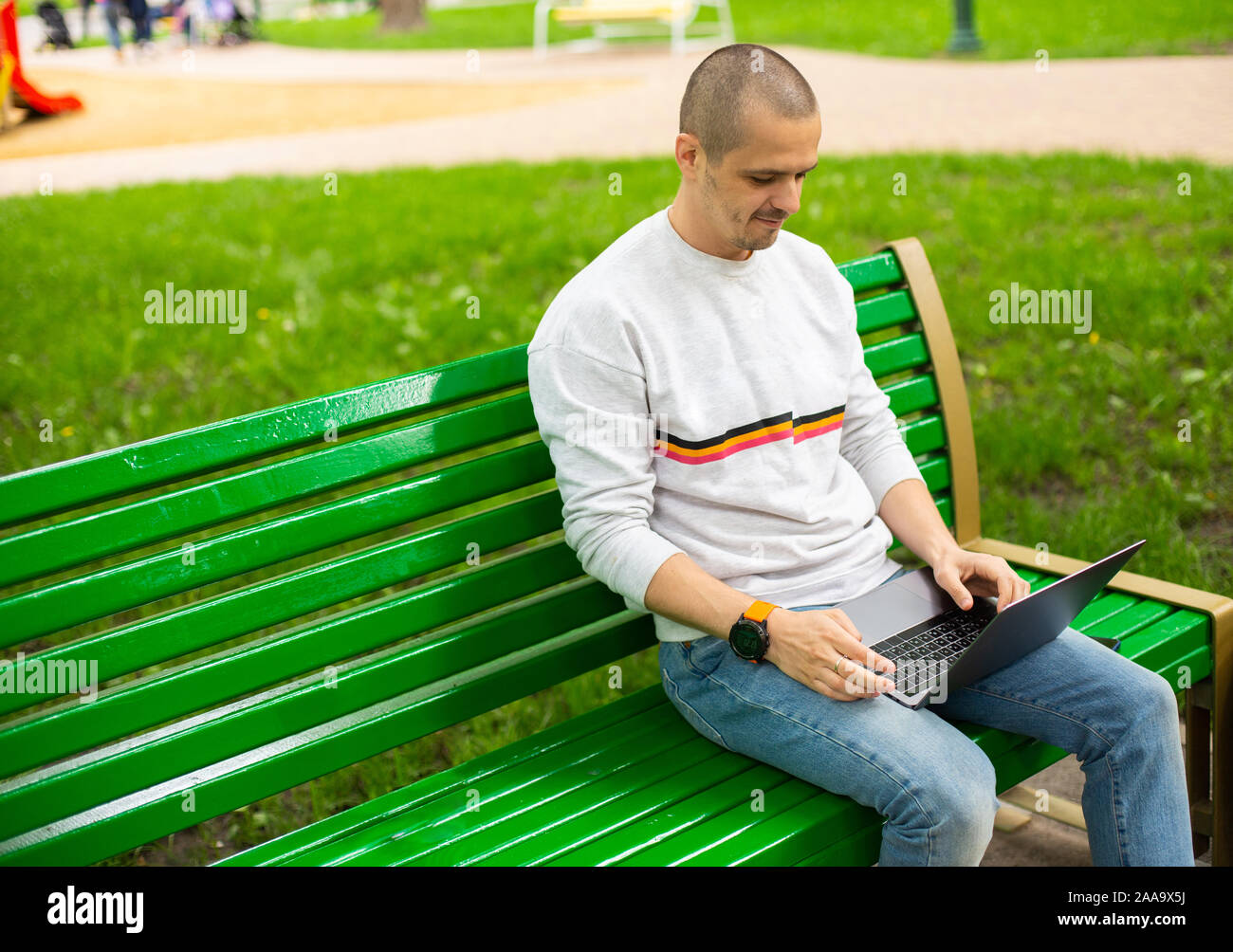 Uomo al lavoro su laptop seduto sulla panchina del parco Foto Stock