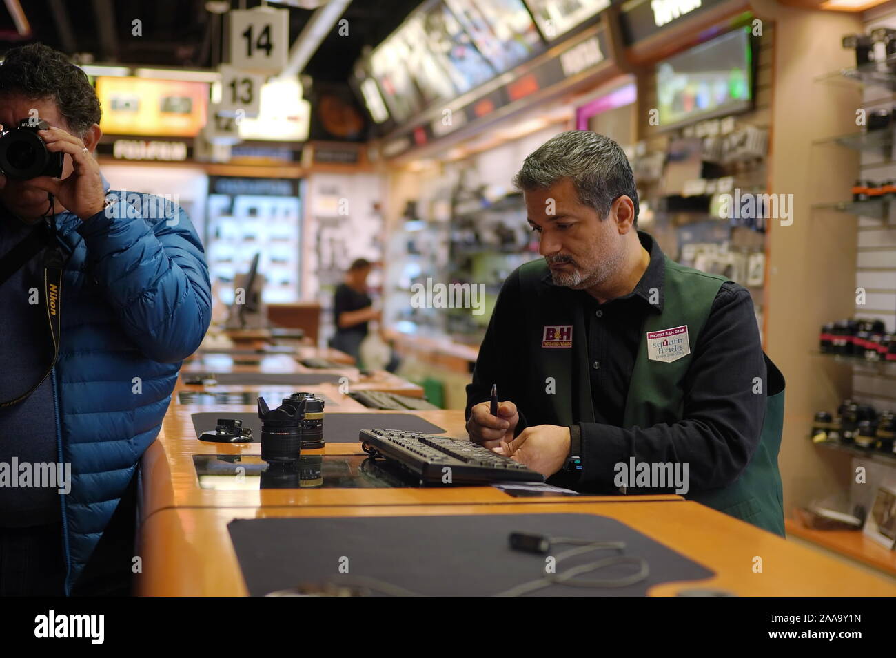 New York, NY / STATI UNITI D'America - 28 Ottobre 2019: Membro di B&H il personale del servizio clienti di aiutare un uomo provare obiettivi e fotocamere presso la postazione di help desk Foto Stock