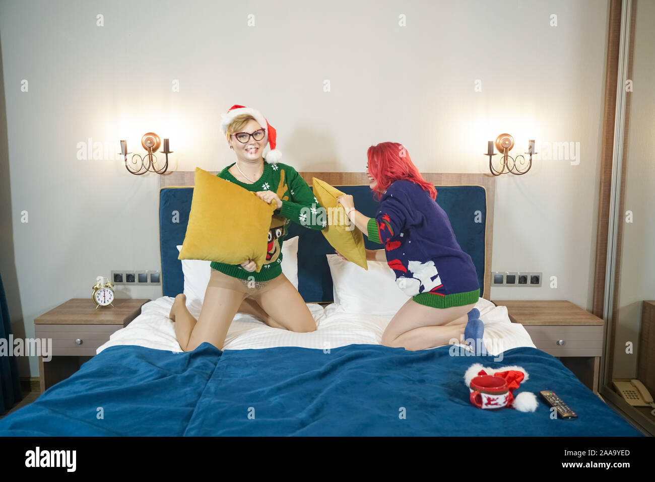 Due cute ragazze felici amici hanno pillow fight in natale maglioni sul big blue bed. Foto Stock