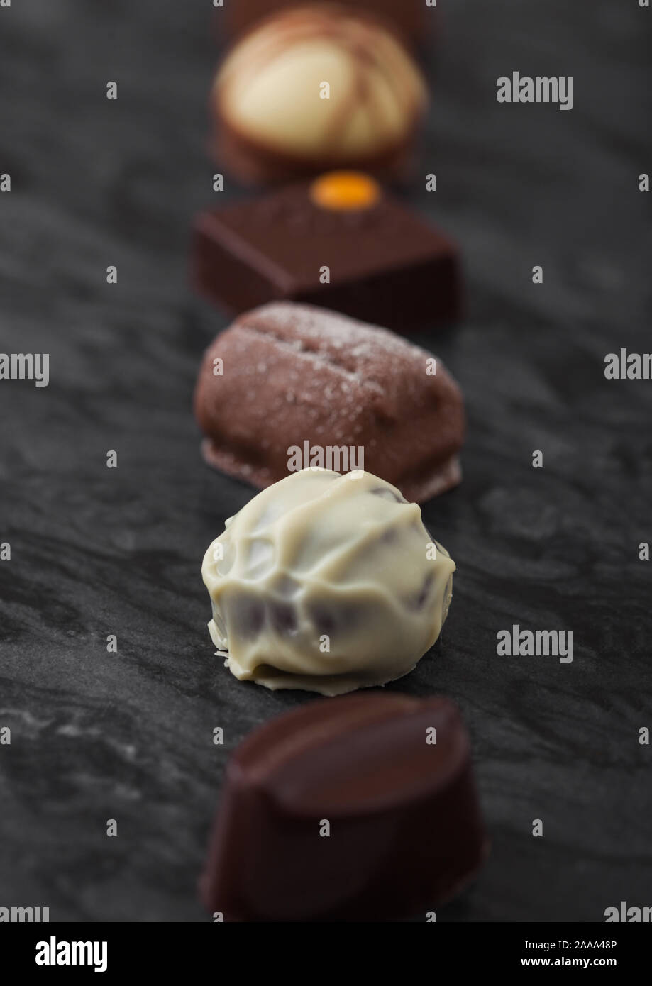 Il lusso di cioccolatini selezione sul pavimento di marmo nero a bordo. Bianco, cioccolato fondente e al latte assortimento. Macro Foto Stock