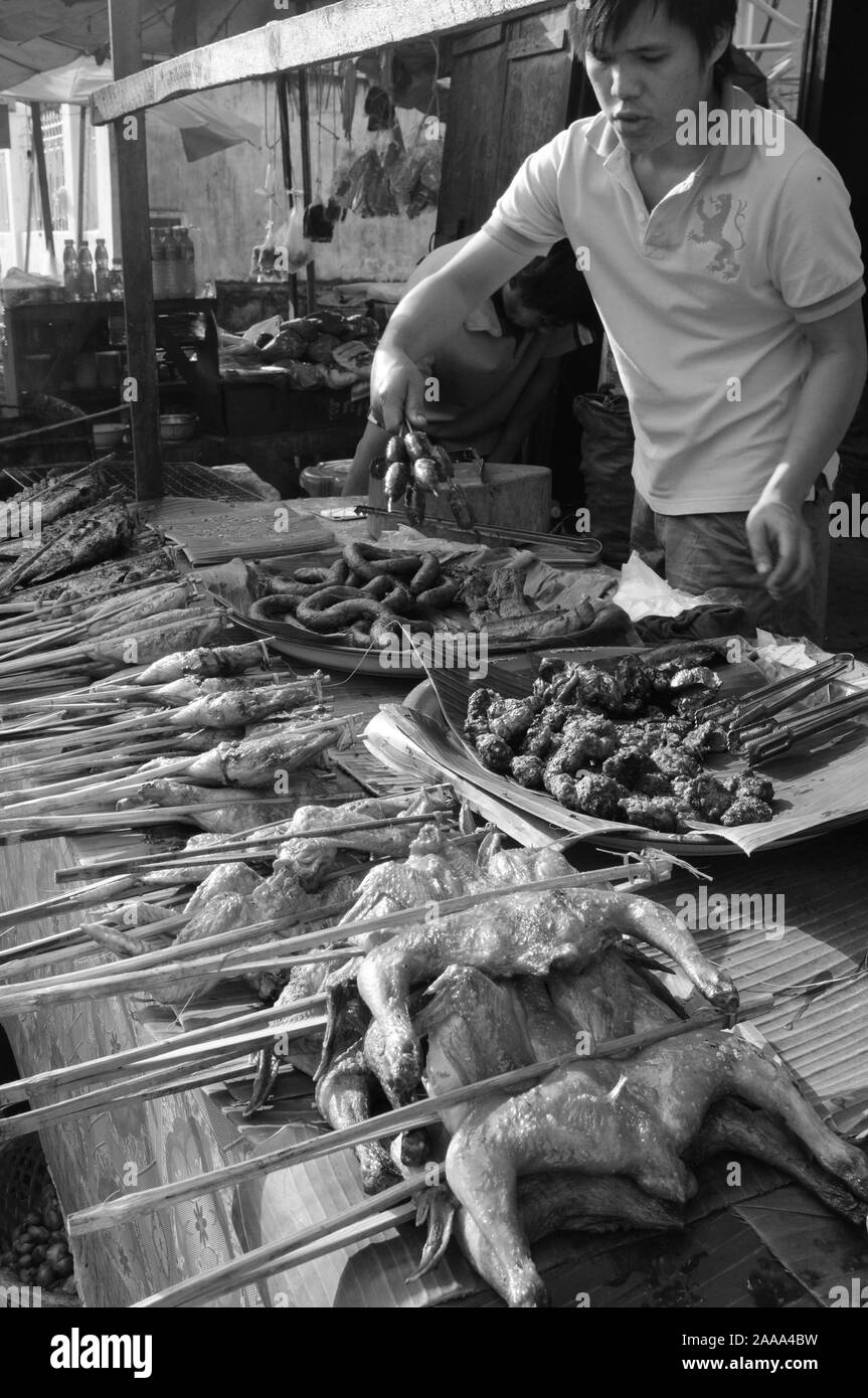 Un giovane uomo di preparare grigliate di pesce e carne al mercato di Luang Prabang City. Foto Stock