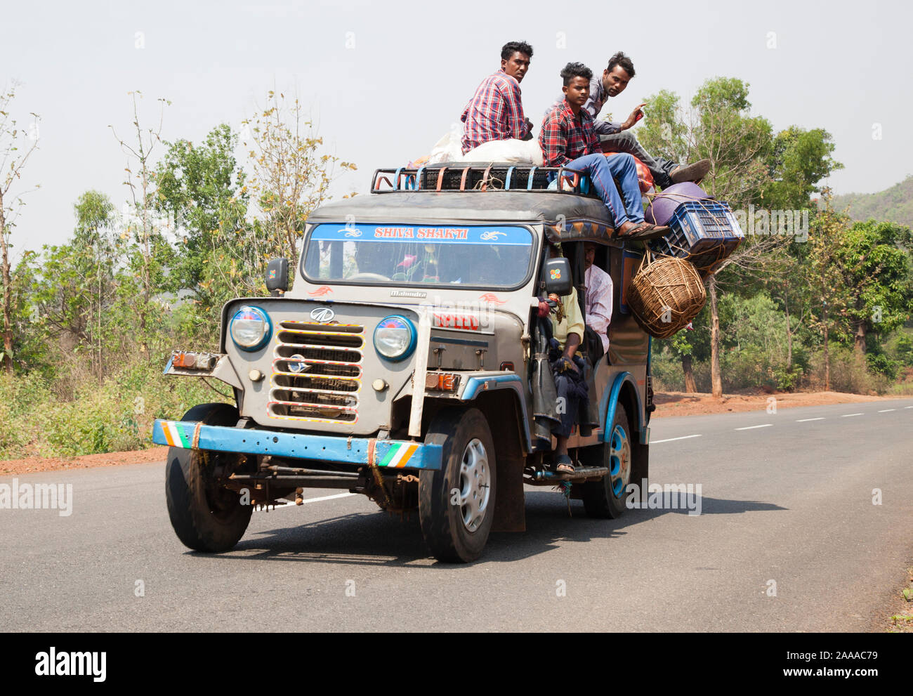 I passeggeri si aggrappano al sovraccarico Indian Mahindra Jeep taxi viaggiano lungo Odisha rurale autostrada Foto Stock