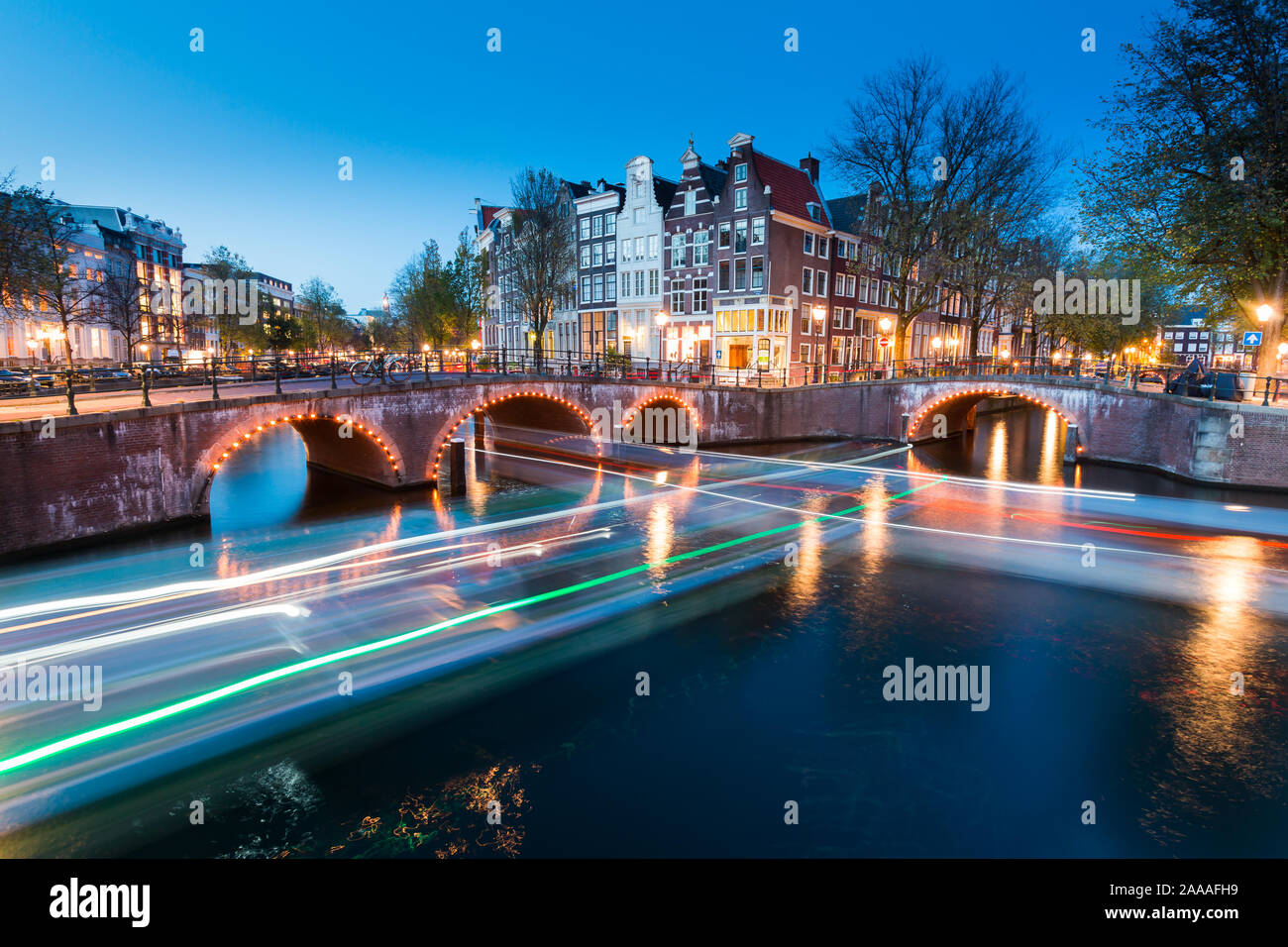 AMSTERDAM, Paesi Bassi - 30 Ottobre 2019: un ponte con luci sopra il canale Keizersgracht durante le ore di colore blu con strisce di luci in barca. Foto Stock