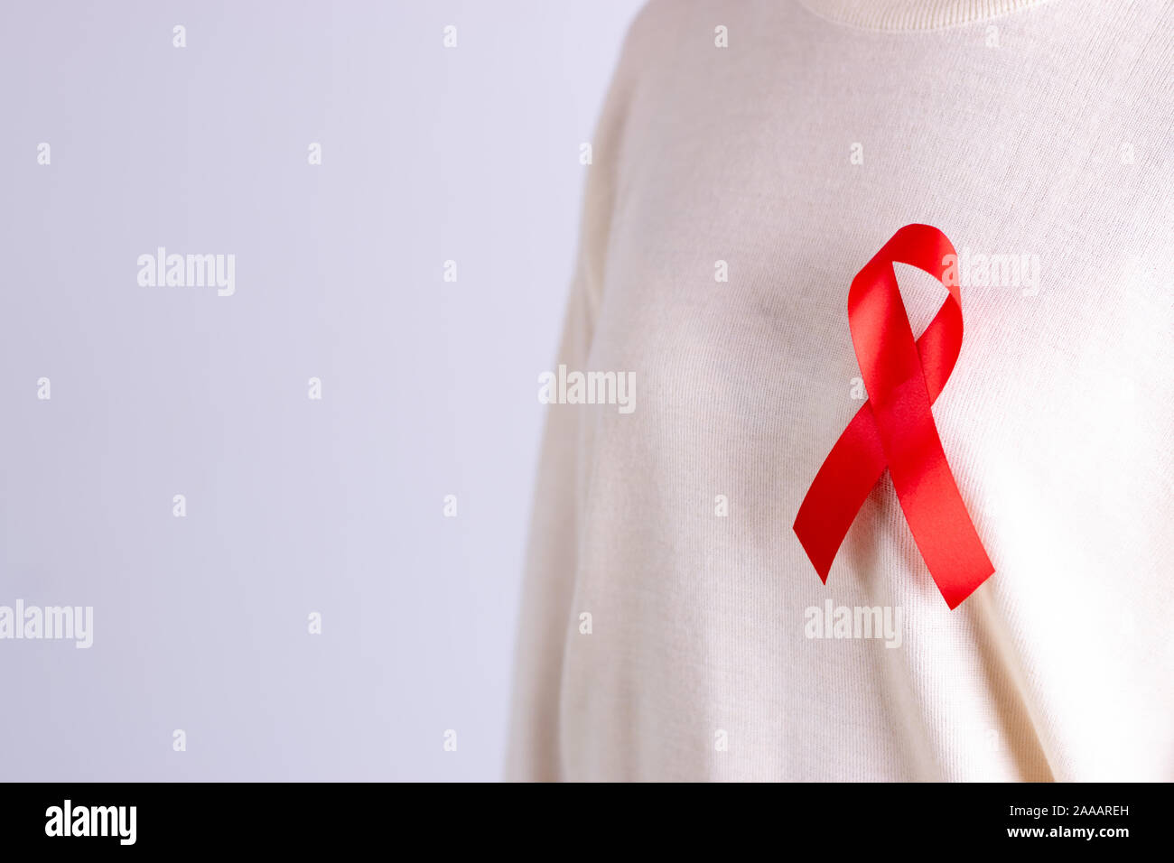 Vista dettagliata del badge rosso nastro sul torace della donna per sostenere il giorno del AIDS. Salute, medicina e consapevolezza del AIDS del concetto. Copia dello spazio. Foto Stock