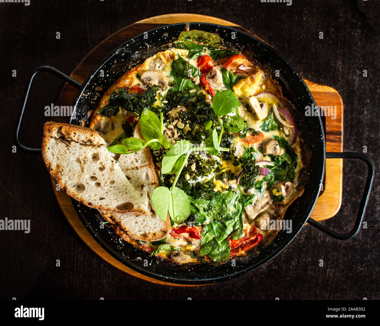 Frittata spagnola prima colazione servita calda in padella con spinaci, funghi, pomodori, formaggi, pane Foto Stock