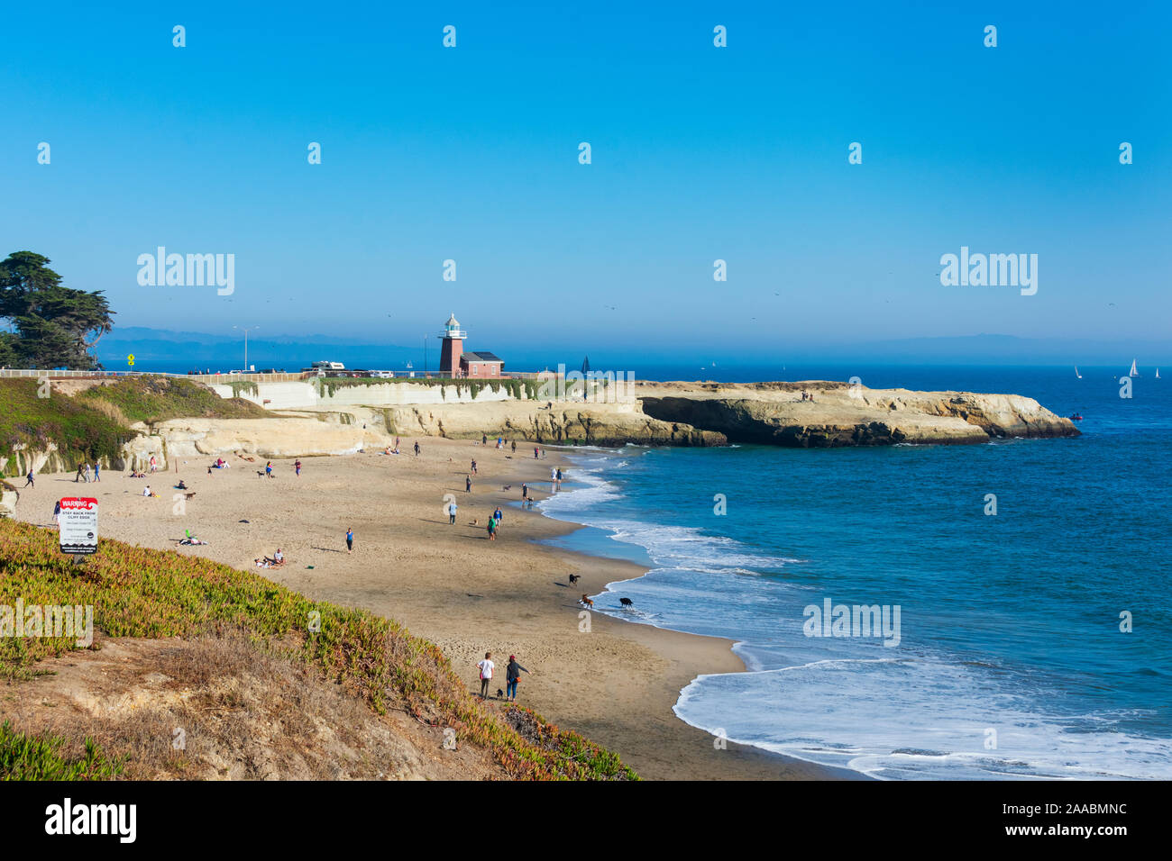 Residenti e visitatori, turisti godetevi le acque dell'Oceano Pacifico sulla sabbiosa spiaggia di cane. Mark Abbott Memorial faro in background. - Santa Cruz, in California, Stati Uniti d'America - 2019 Foto Stock