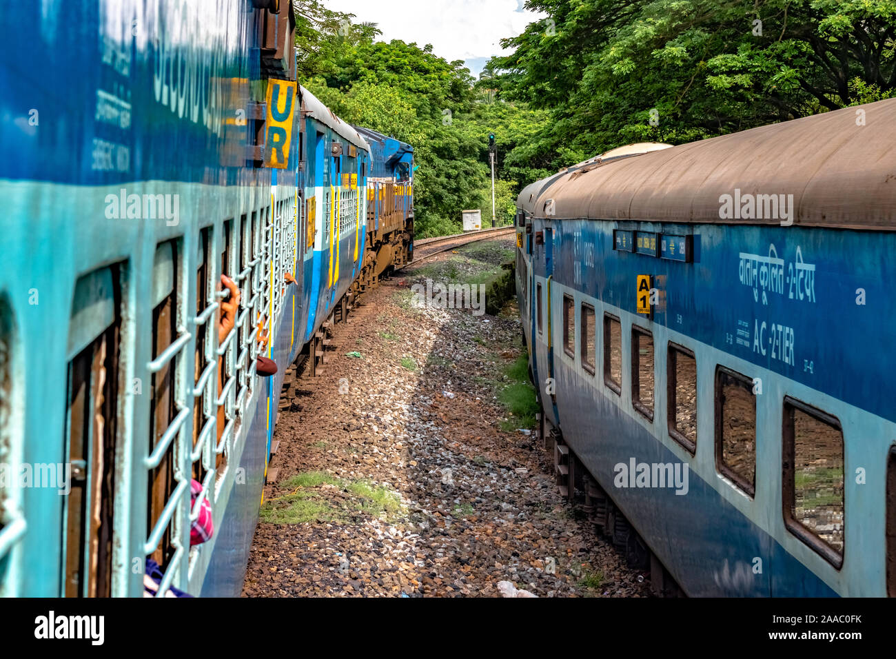 Le ferrovie indiane Treno in partenza a ritmo lento, attraversando un altro treno in esecuzione parallela ad essa in direzione opposta, immerso nel verde di i Ghati Occidentali. Foto Stock