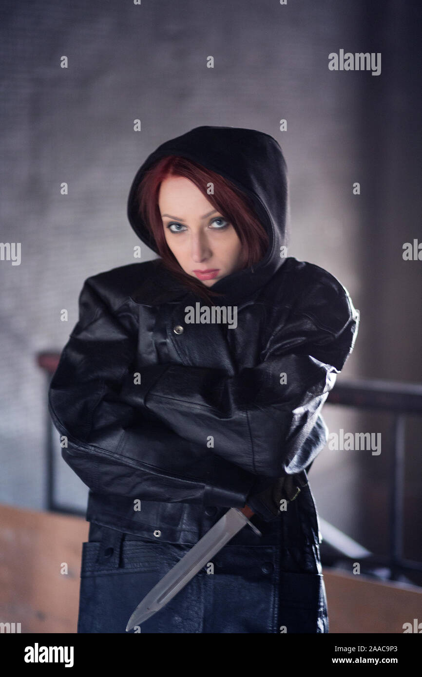 Brutale ragazza in un ampio mantello nero con un coltello di grosse dimensioni nelle sue mani. Foto Stock