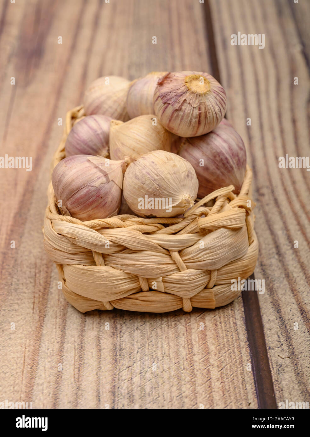 A pochi capi di giovani aglio in un cesto di vimini su un sfondo di legno. Raccolto autunnale. L'agricoltura moderna. Close up Foto Stock