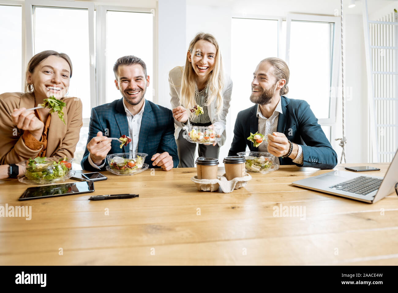 Il gruppo di un ufficio di giovani lavoratori di mangiare insalate e di bere il caffè all'ufficio moderno mensa. Concetto di un sano cibo da asporto sul lavoro Foto Stock