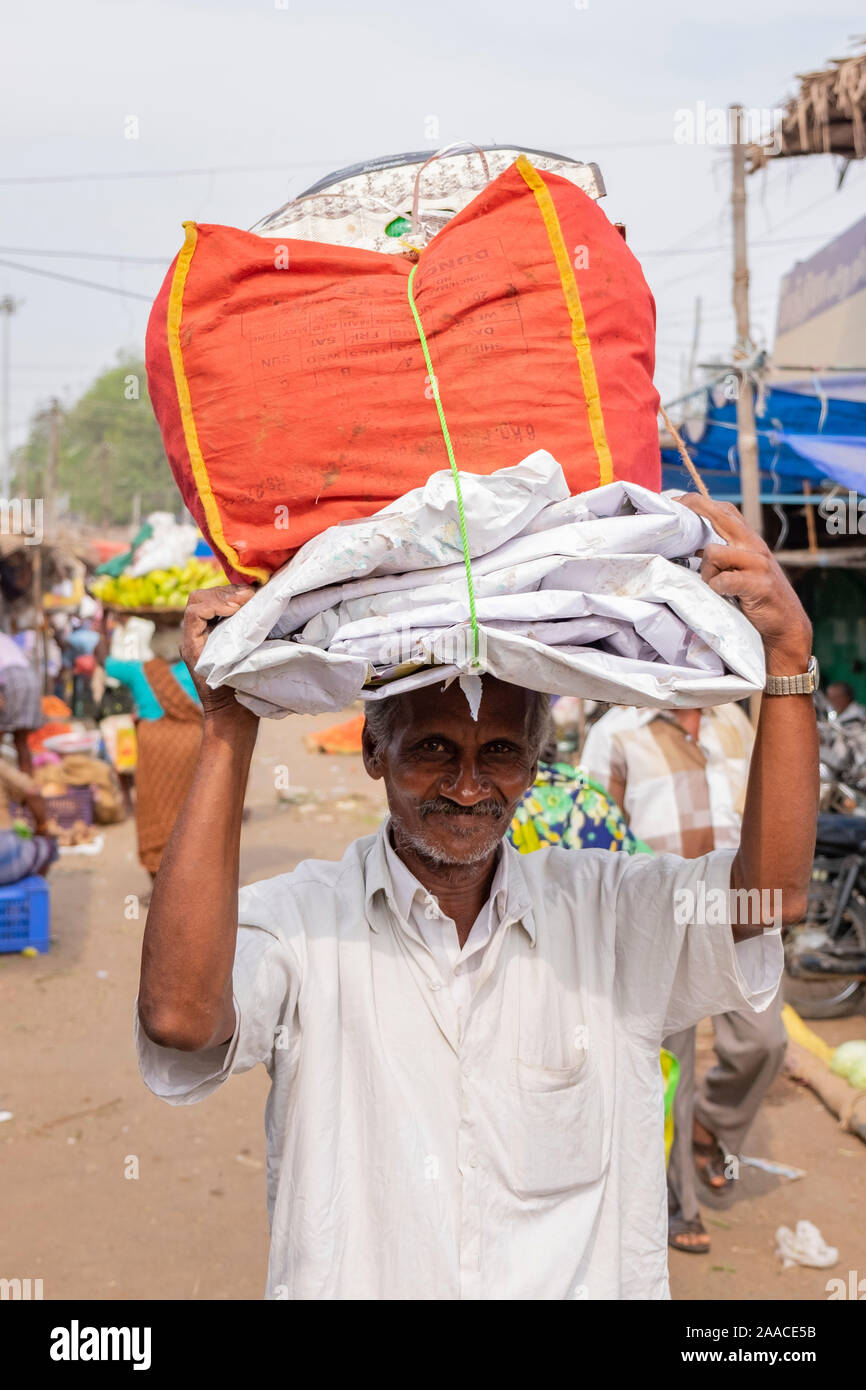 Il vecchio uomo portante avvolto il pacco di plastica sulla sua testa al mercato all'aperto in Tiruchirappalli, Tamil Nadu, India Foto Stock