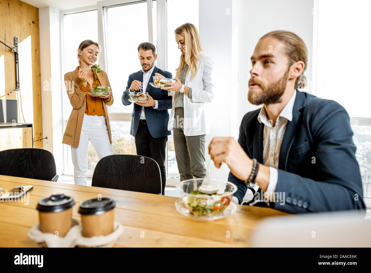 Il gruppo di un ufficio di giovani lavoratori di mangiare insalate e di bere il caffè all'ufficio moderno mensa. Concetto di un sano cibo da asporto sul lavoro Foto Stock