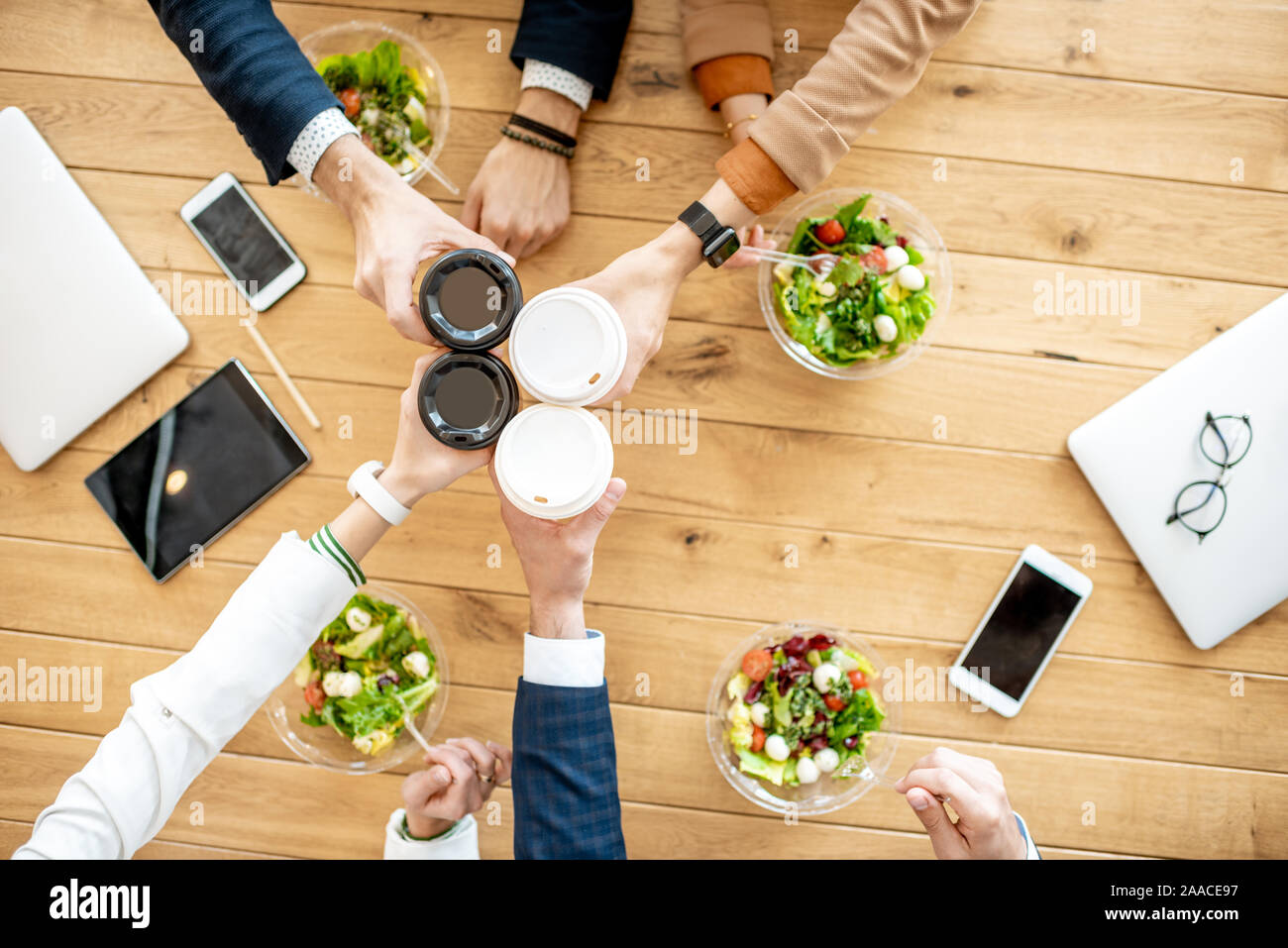 Ufficio lavoratori tintinnio tazzine di caffè durante un pranzo di lavoro con le insalate sane, vista da sopra il tavolo in legno Foto Stock