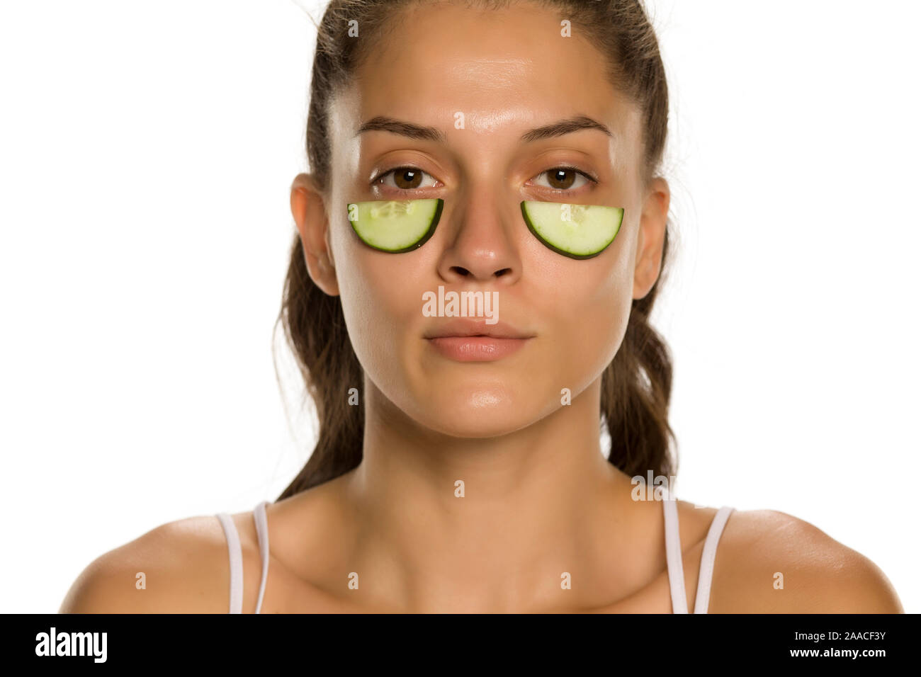 Giovane donna in posa con fette di cetrioli undeer i suoi occhi su sfondo bianco Foto Stock
