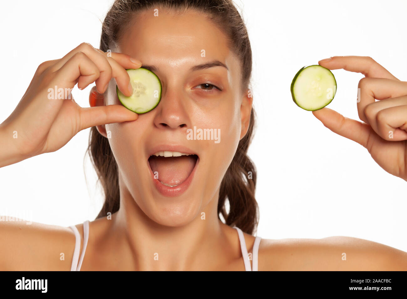 Giovane donna sorridente in posa con fette di cetrioli su i suoi occhi su sfondo bianco Foto Stock