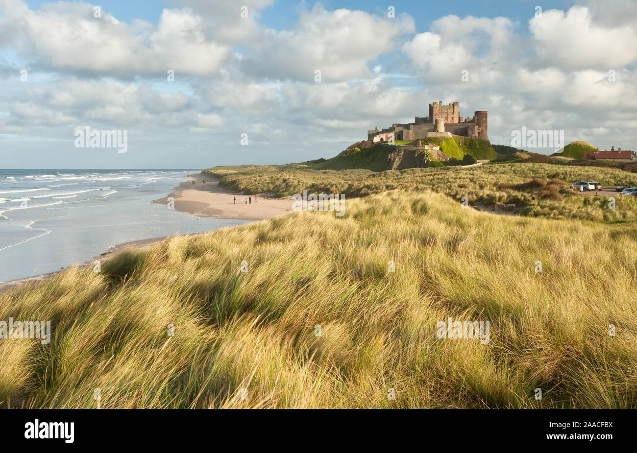 Il castello di Bamburgh arroccato su balze rocciose che si affaccia su dune costiere, la spiaggia e il Mare del Nord. Northumberland, Inghilterra Foto Stock