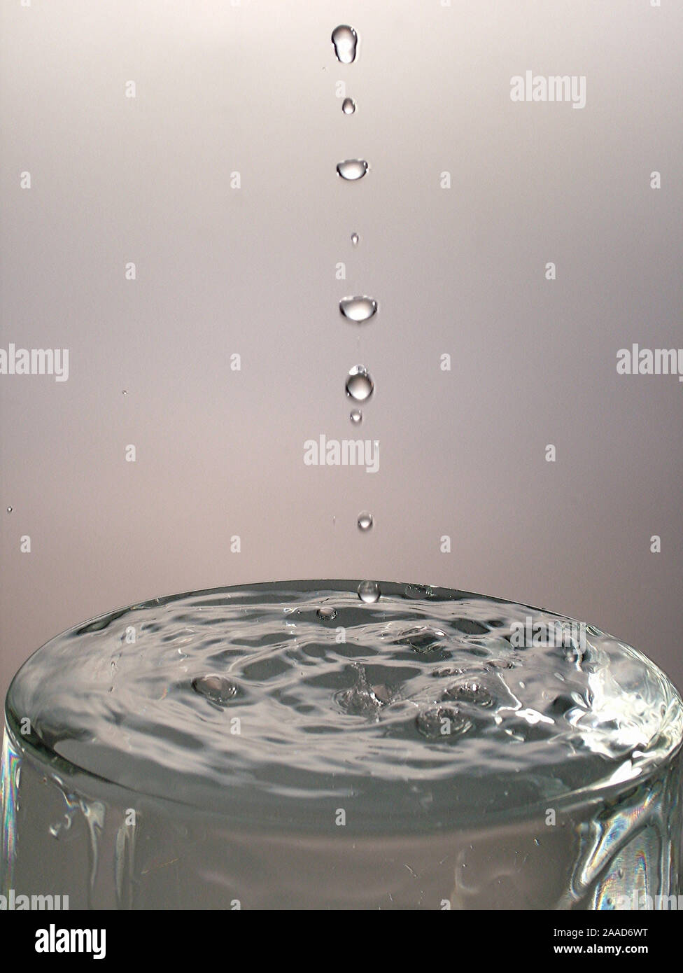 Gocce che cadono nel bicchiere pieno di acqua Foto stock - Alamy
