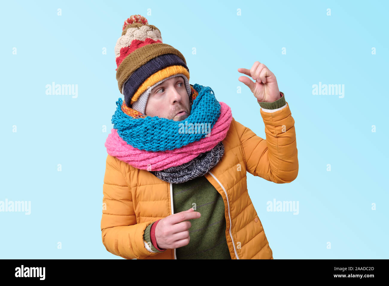 Bello caucasian funny man in vari cappelli e sciarpe mostrando piccole quantità con il dito. Studio shot Foto Stock