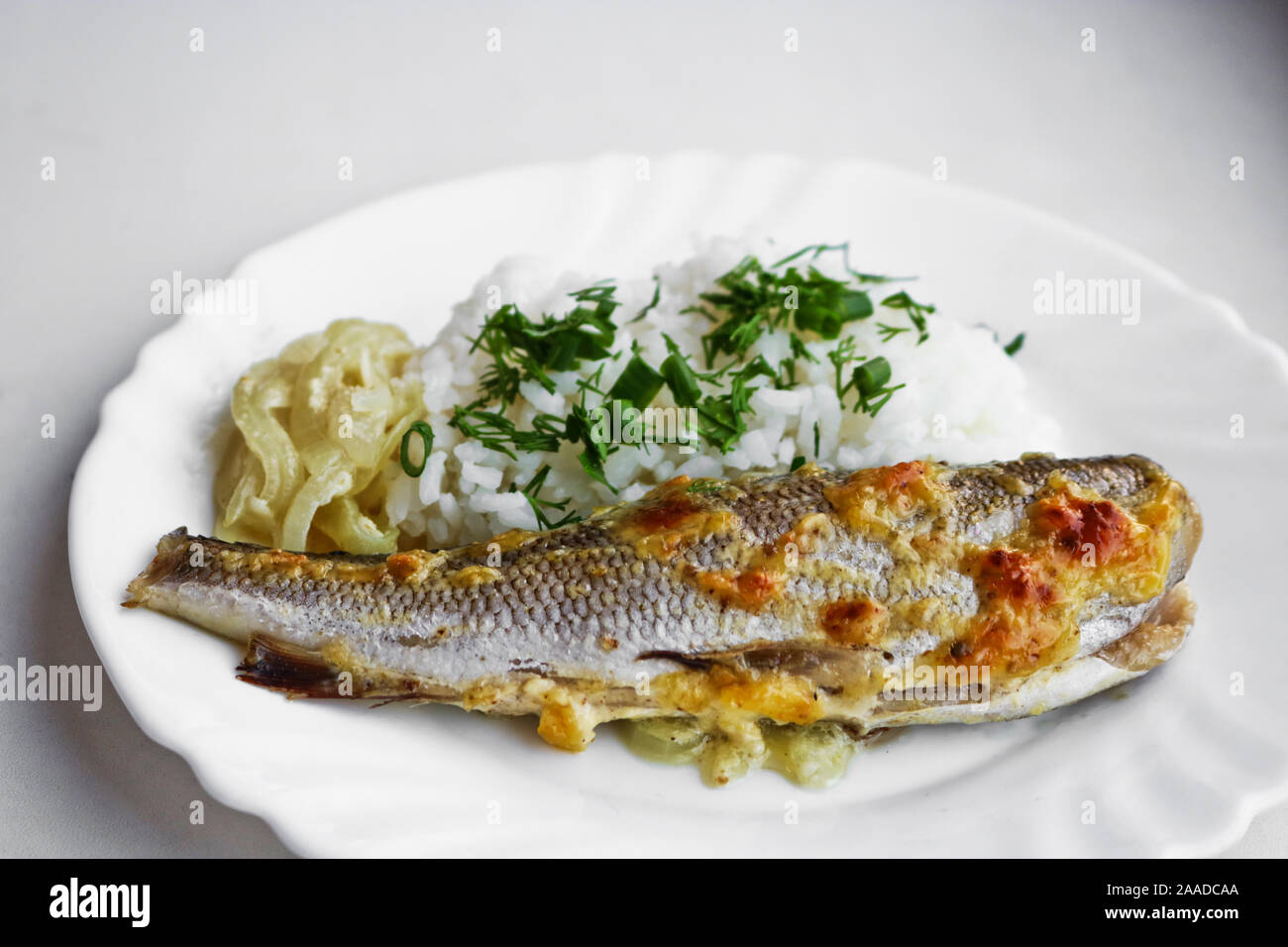 Pesce al forno con riso bollito e cipolle fritte su un piatto bianco. Una sana dieta alimentare. Foto Stock