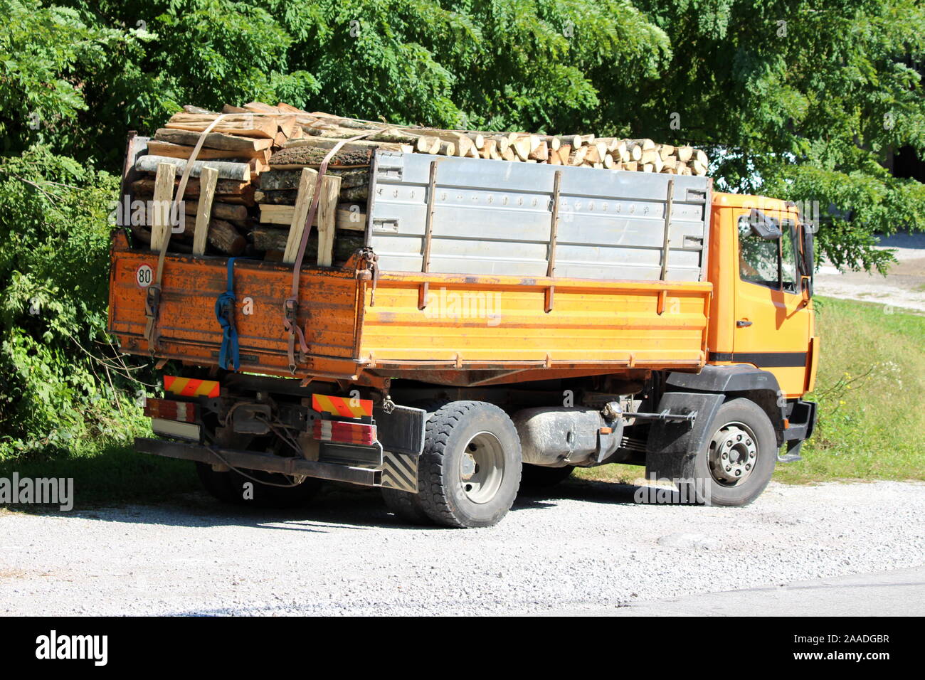 Vista posteriore del vecchio camion giallo riempito con legna da ardere  parcheggiato sulla ghiaia parcheggio accanto alla strada asfaltata  circondata da alberi fitti sul caldo estivo soleggiato Foto stock - Alamy