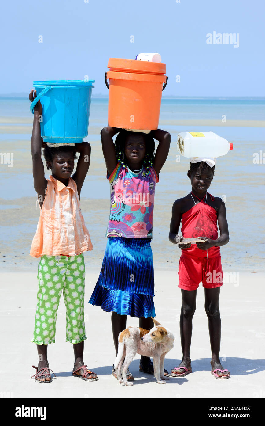 Ritratto di tre ragazze, con i contenitori sulla testa di raccogliere acqua e cane, Orango Isola, Bijagos Riserva della Biosfera dall'UNESCO, Guinea Bissau, febbraio 2015. Foto Stock