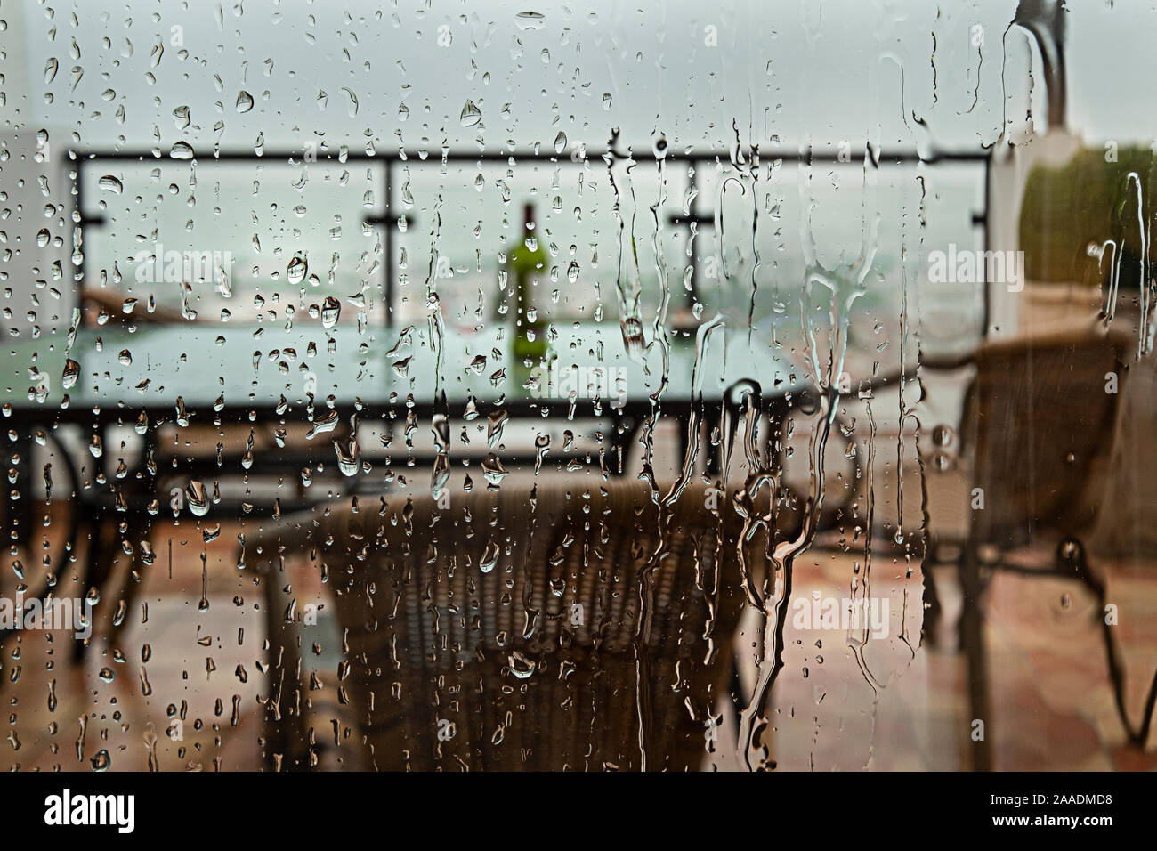 Vista attraverso un vetro ricoperto con le gocce di pioggia sulla terrazza arredata durante la stagione delle piogge a Nerja, Spagna Foto Stock