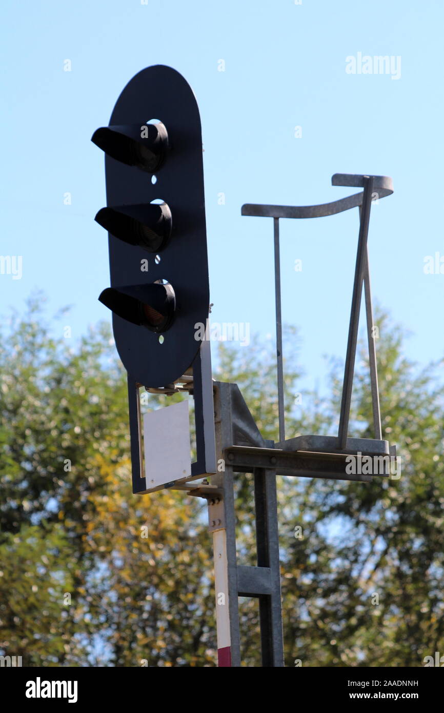I binari ferroviari semaforo montato su robusto telaio metallico con lo spintore di sicurezza circondato da alberi e cielo blu chiaro su caldo e soleggiato giorno di estate Foto Stock