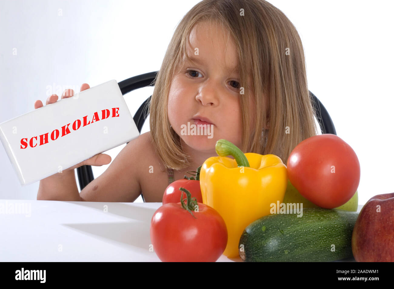 Vierjähriges Mädchen hält Schokoladentafel in der mano und sitzt vor Gemüse und Obst (modell rilasciato) Foto Stock