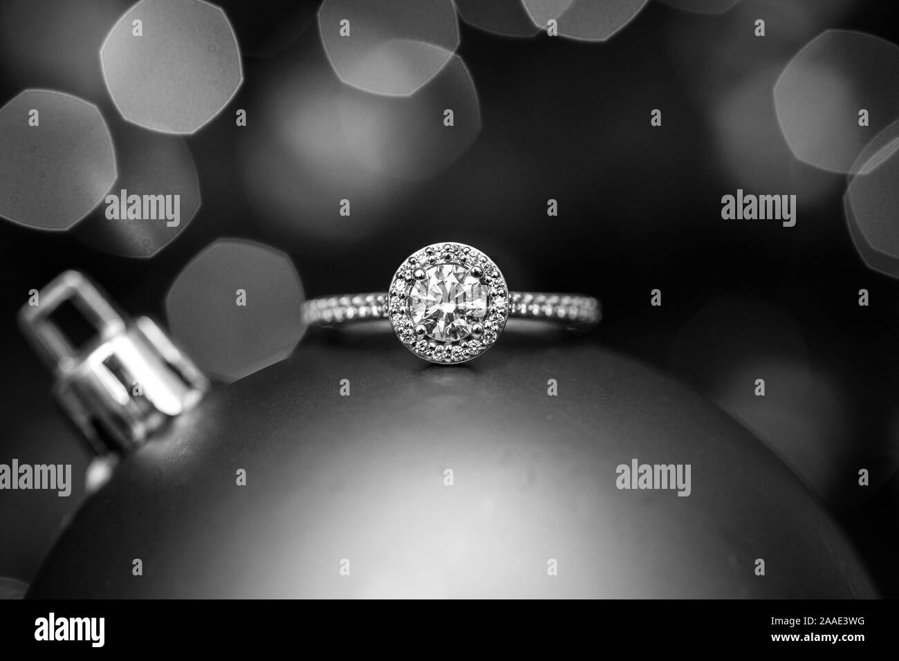Anello di fidanzamento su un ornamento di Natale con le luci in background. In bianco e nero. Foto Stock