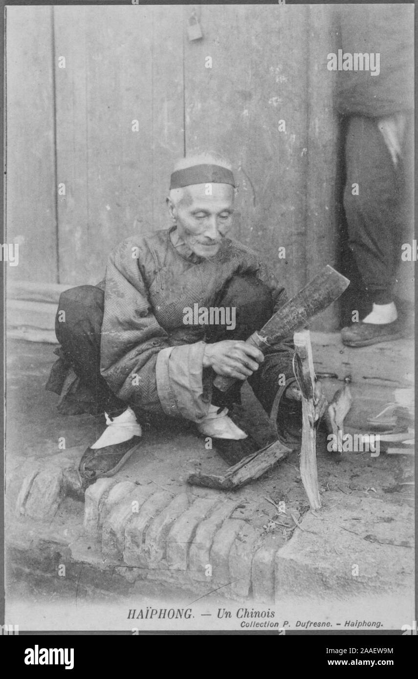 Cartolina inciso di un uomo anziano squatting dal lato della strada la trinciatura di un bastone, Haiphong, Vietnam, dal fotografo P. Dufresne, 1908. Dalla Biblioteca Pubblica di New York. () Foto Stock