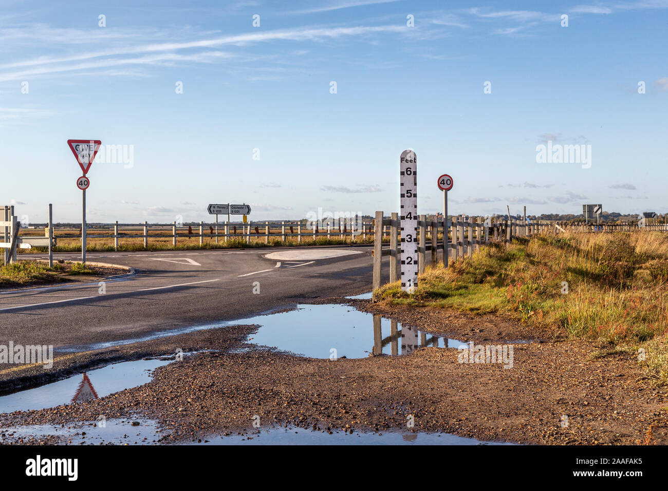 La causeway sulla Mersea isola conosciuta come Strood è coperto da acqua di mare due volte al giorno. In primo piano un marcatore di profondità può essere visto. Foto Stock