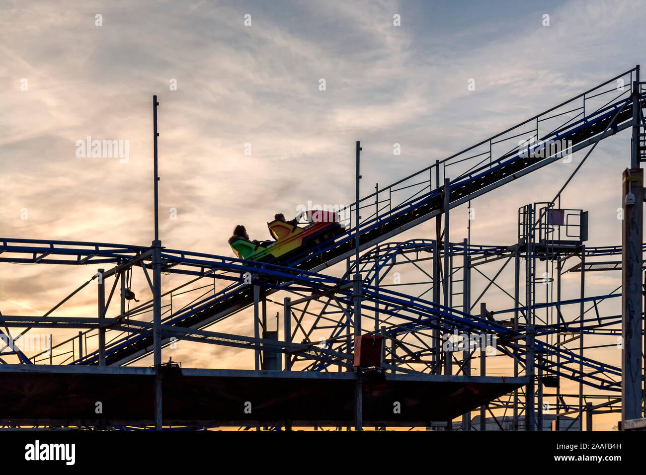 Un roller coaster sale su una pendenza ripida mentre piloti tenere la barra di sicurezza in previsione della caduta. Impostare contro un bel cielo d'oro. Foto Stock