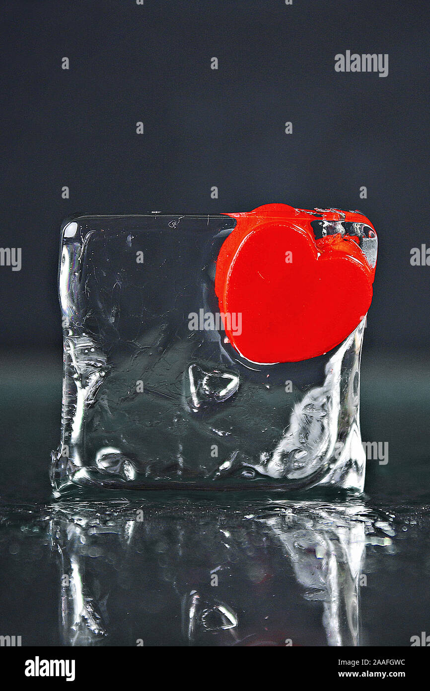 Un piccolo cuore rosso congelato in un cubetto di ghiaccio. Ghiaccio fondente, acqua Foto Stock