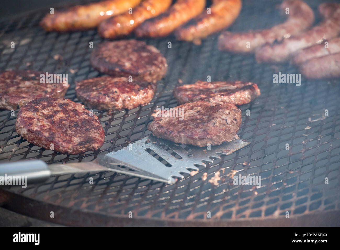 Spatola in acciaio capovolgimento di un hamburger patty essendo cotti su una griglia aperta Foto Stock