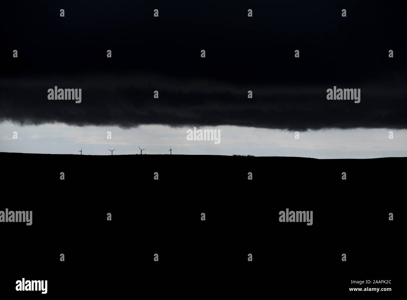 Distanti le turbine eoliche sulla Canadian Prairies stagliano contro una sottile fascia di cielo blu con nuvole temporalesche tettuccio Foto Stock