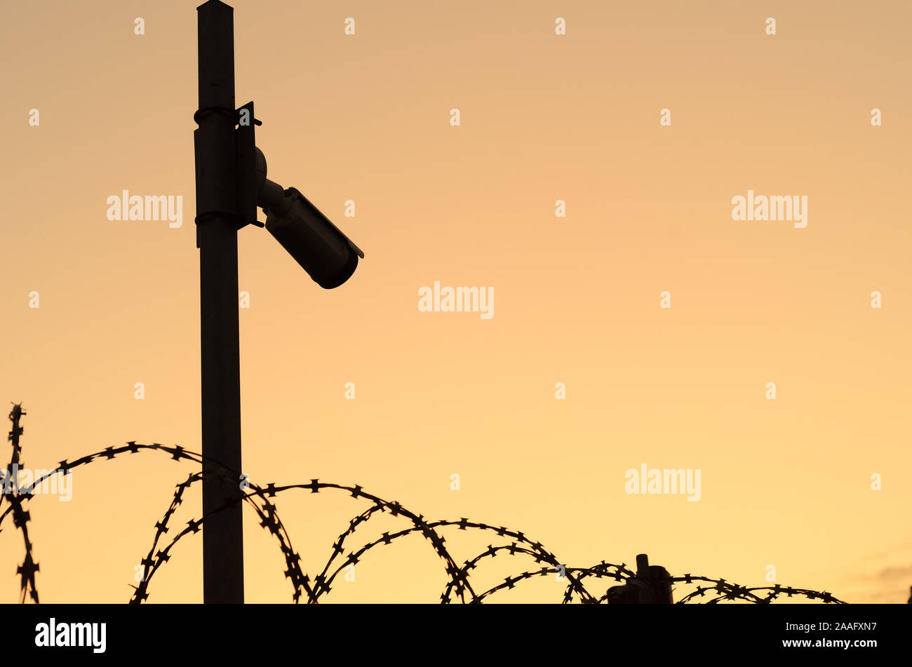 Silhouette della videocamera di sicurezza sul palo su sunset.Osservazione del perimetro dell'area protetta con filo spinato.Spazio per il testo Foto Stock