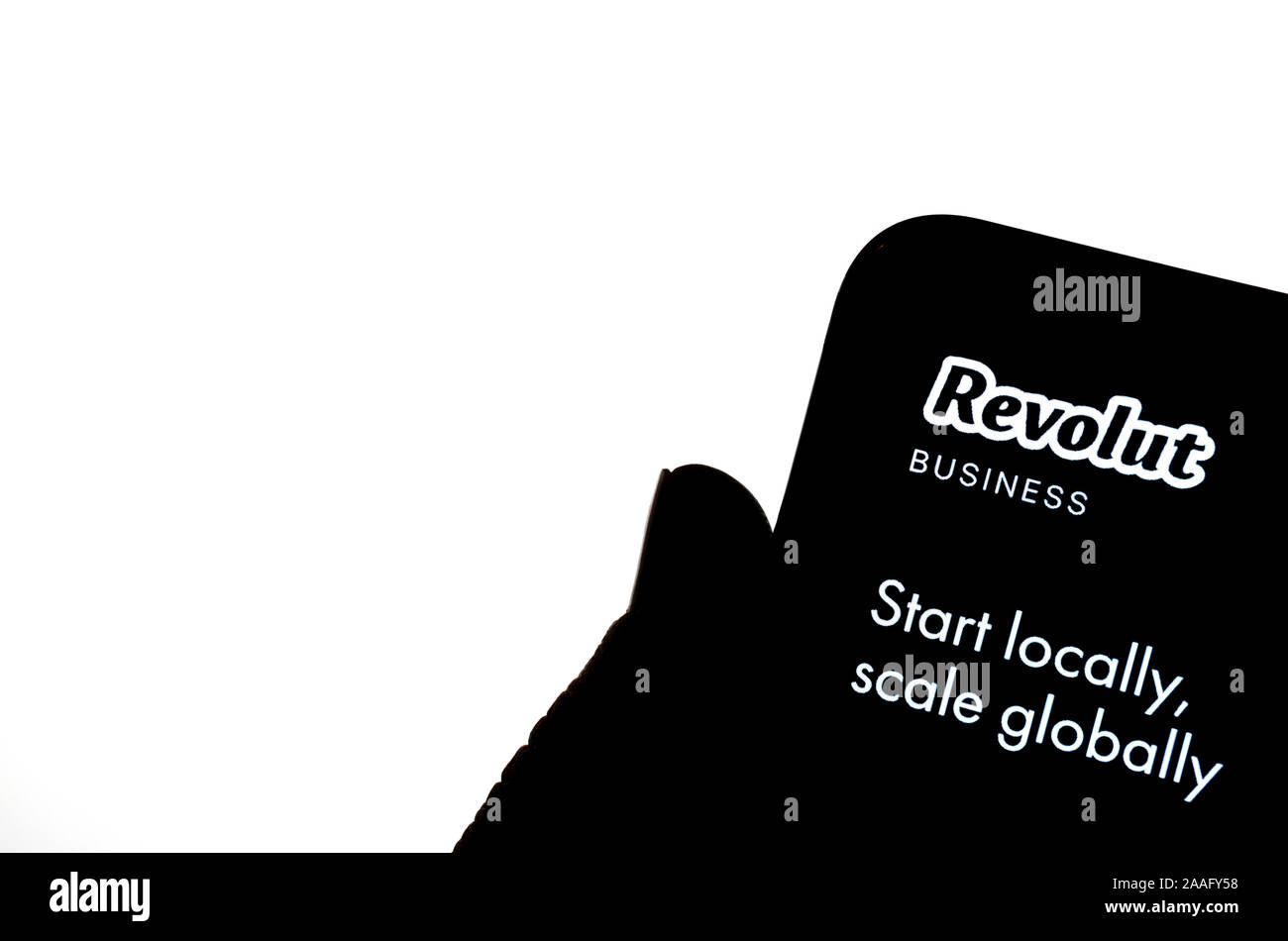 Revolut app aziendali sullo smartphone attesa da una silhouette di una mano davanti a schermo bianco. Foto Stock